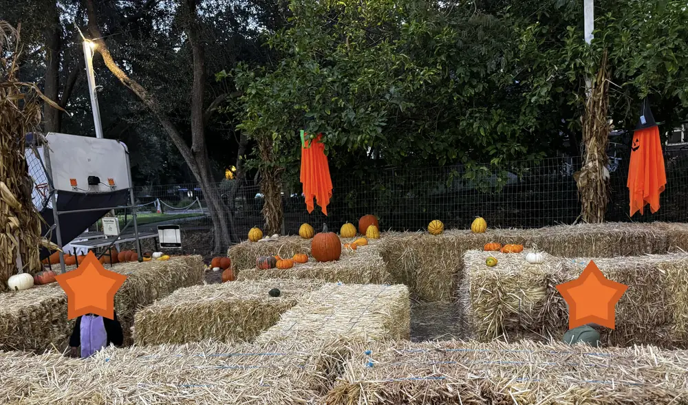 A hay-bale maze decorated with pumpkins and orange ghosts hanging from the trees, at dusk